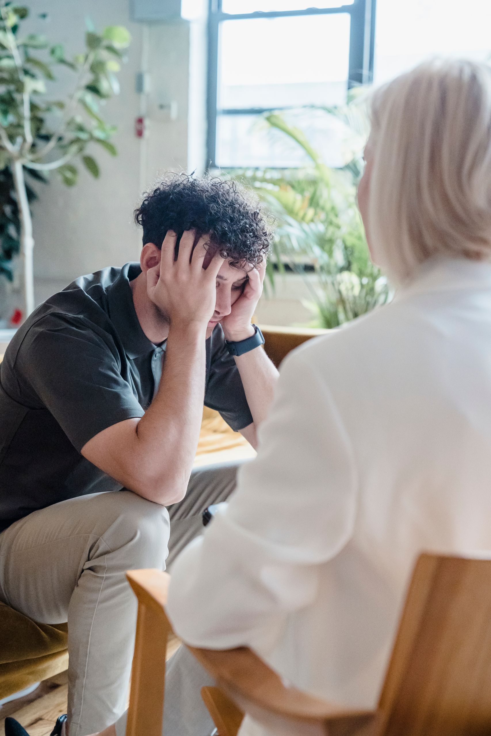 A young man in therapy, sitting and looking distressed, during a psychological session.